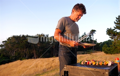 Man barbequing kebabs in the evening on rural property