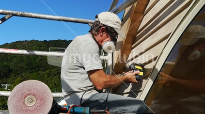 Man sanding house with mask and scaffold railings for protection