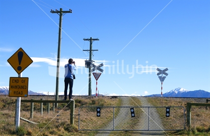 Railway line warnings, lamp posts and tourist photographer standing on post.