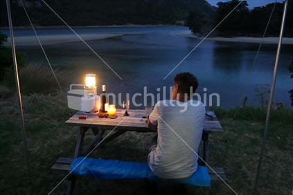 Man sitting under tent awning with wine and camping lantern