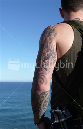 Tattooed arm of a man looking out to sea
