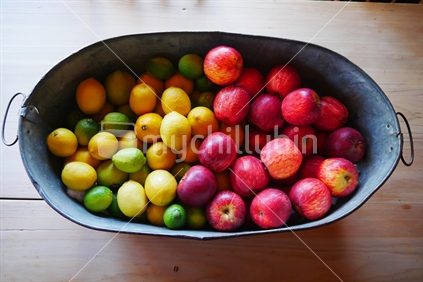 A metal bucket full of apples and lemons