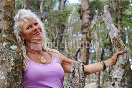 Radiant aging woman amongst tree trunks in native bush