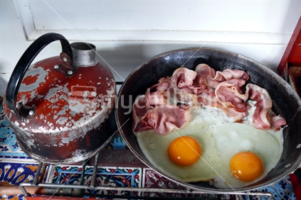 Bacon and eggs camp cookup with old kettle on primus stove