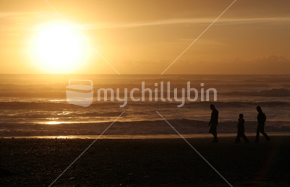 A family walks along the beach at sunset