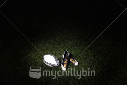 Rugby boots and a ball rest on a field at night.