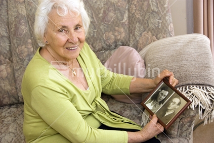 Sweet elderly widow holding af frame with images of herself and her deceased husband as a young couple