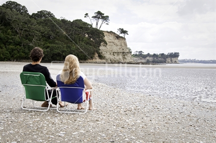 Young couple in beach chairs, Long Bay, Auckland, New Zealand
