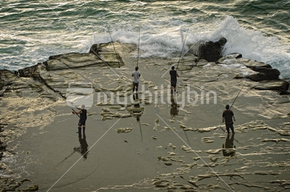 Four fishermen fishing from rocks at Muriwai surf beach
