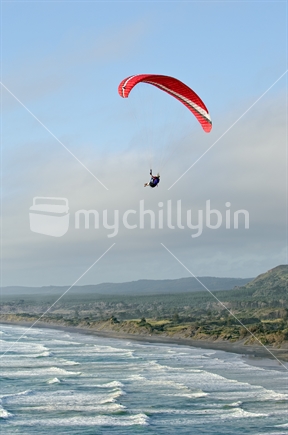 Paragliding flying high over muriwai surf beach