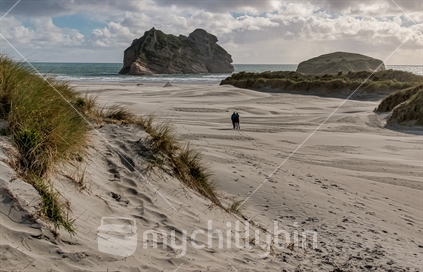 Large expansive sandy beach with couple walking and offshore island.