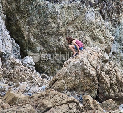 Girl peering into cave in cliff face.