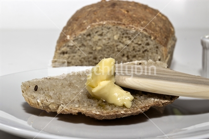 Fresh bread being spread with butter. 