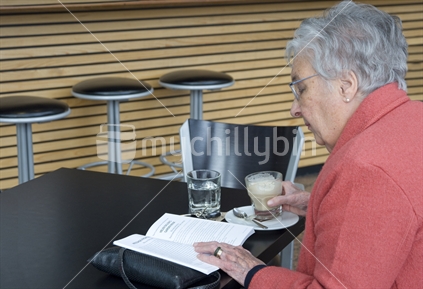 Retired elderly woman reading in cafe while having coffee
