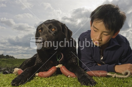 12 year old Chinese boy and black Labrador laying in the grass