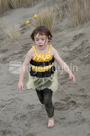 Little girl (7 years old) dressed in bumble bee costume playing at the beach