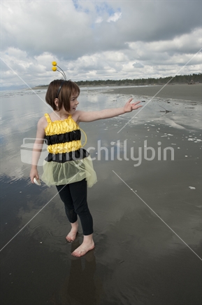 Little girl (7 years old) dressed in bumble bee costume playing at the beach