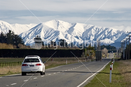 Car driving down Route 72 in Canterbury towards snow-capped Southern Alps