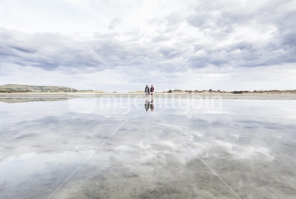 Reflection of young couple holding stick above their heads on Catlins estuary