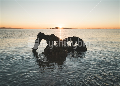 Sunrise over silhouetted wreckage in Hauraki gulf Auckland
