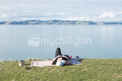 Young adult woman resting on picnic blanket with scenic water backdrop