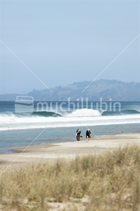 Couple walking along surf beach on summer day, Auckland region