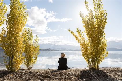 Woman relaxing by Lake Wanaka on a calm Autumn day
