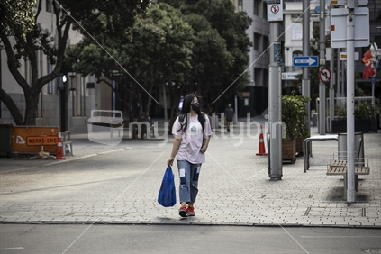 Female walking through empty street while wearing PPE face mask