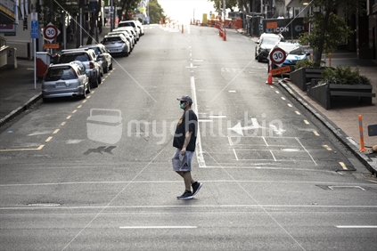 Male walking through empty street while wearing face mask