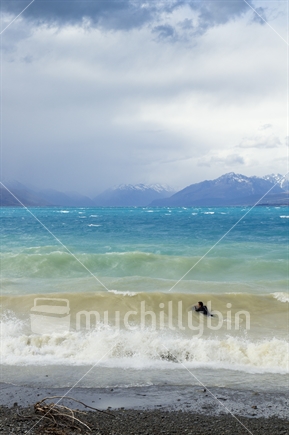 Person body boarding on Lake Pukaki, in stormy weather, below the snow capped Southern Alps mountains.