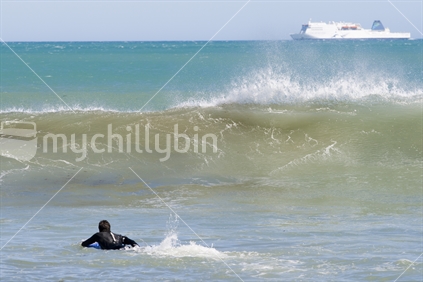 Surfer paddling out at Wellington's Houghton Bay, with the InterISlander in the distance. 