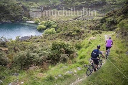 male and female mountain bikers, cycling downhill near lake wanaka
