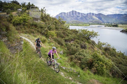 male and female mountain bikers, cycling downhill near lake wanaka