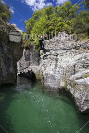 adventurous female jumps from cliff at Motatapu Gorge, Southern Lakes, South Island