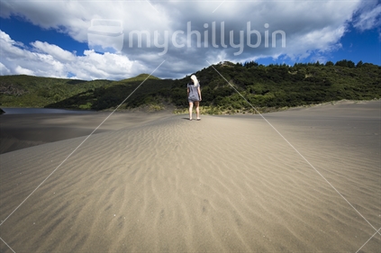 Female walking along black sand dunes near Lake Waimanu, Bethells beach, Auckland