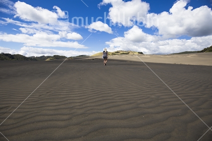Black sand dunes and female walking in distance near Lake Waimanu, Bethells beach, Auckland