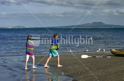 Two young girls on beach with Rangitoto Island in background