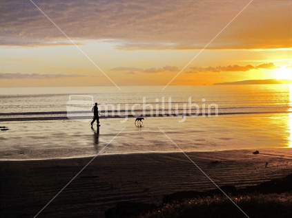 Man and dog walking on Orewa beach, at sunrise.