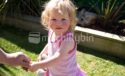 Little girl holding onto daddy's finger in a New Zealand backyard