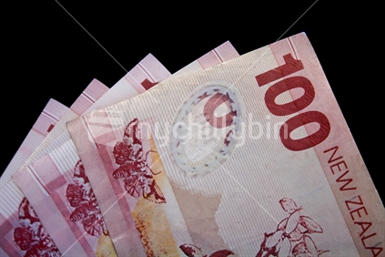 Several New Zealand $100 notes against black background.