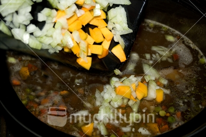 Adding chopped onion and pumpkin to a chunky homemade soup.