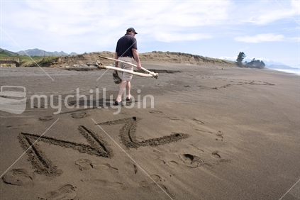 Man collecting driftwood. "NZ" written in sand in foreground.