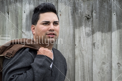 Man holding jacket, in relaxed pose against a wooden fence