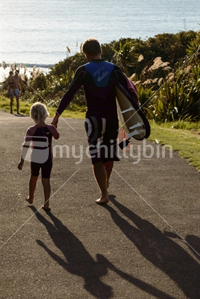 Father and child walk down to a surf beach