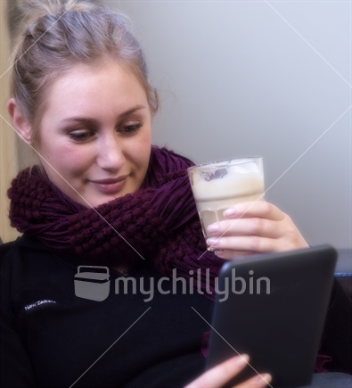 Young woman reading on an e-reader while drinking coffee