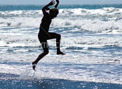 Teenager leaping through shallow waves