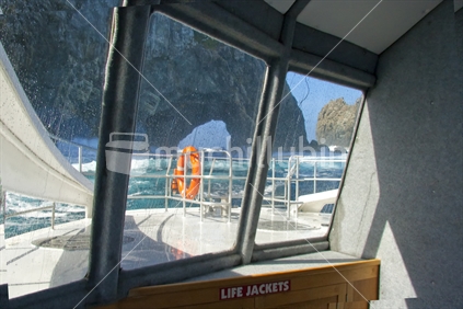 A big sea, life jackets, life buoy, and a view through the widow of a launch approaching the hole in the rock, Bay of Islands, New Zealand.