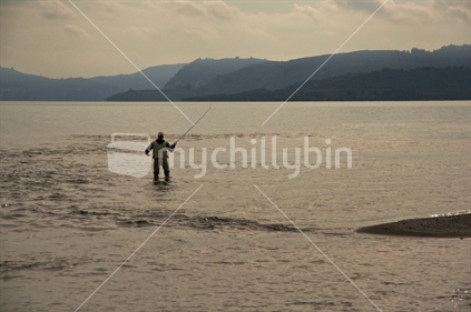 A trout fisher at the mouth of the Waitahanui river, lake Taupo, New Zealand (foreground focus).