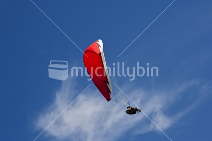 Red paraglider from below in the blue Taranaki sky with one white cloud
