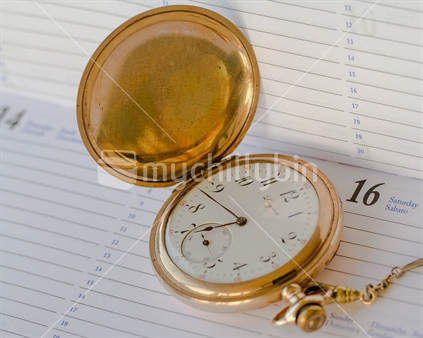 An antique gold pocket watch sitting on a diary.